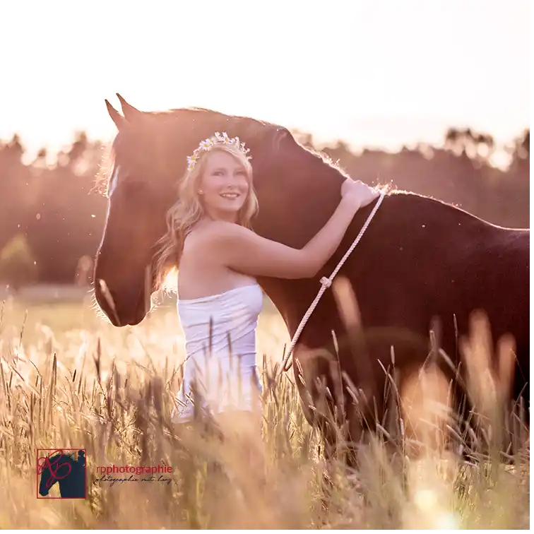 Frau kuschelt im Sonnenuntergang mit ihrem Pferd auf einem Feld