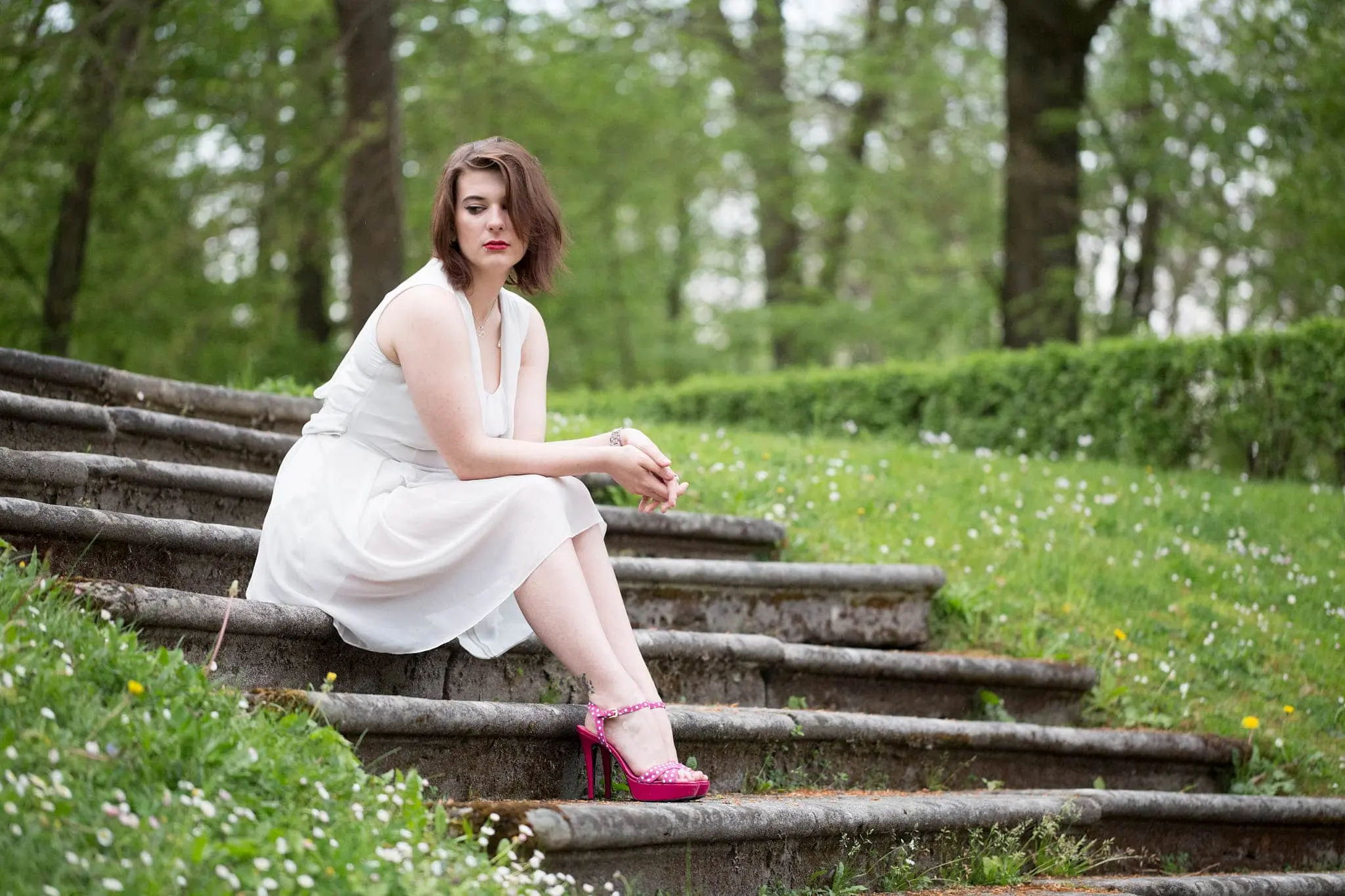 Junge Frau im weißen Kleid sitzt auf einer Treppe im Schlossgarten