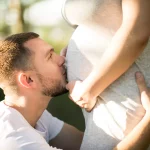 Ein junger Vater küsst den Bauch seiner schwangeren Frau