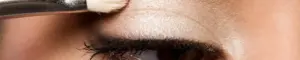 Ein Detail von dem Gesicht einer Frau, die sich mit einem Pinsel gerade die Augen schminkt.